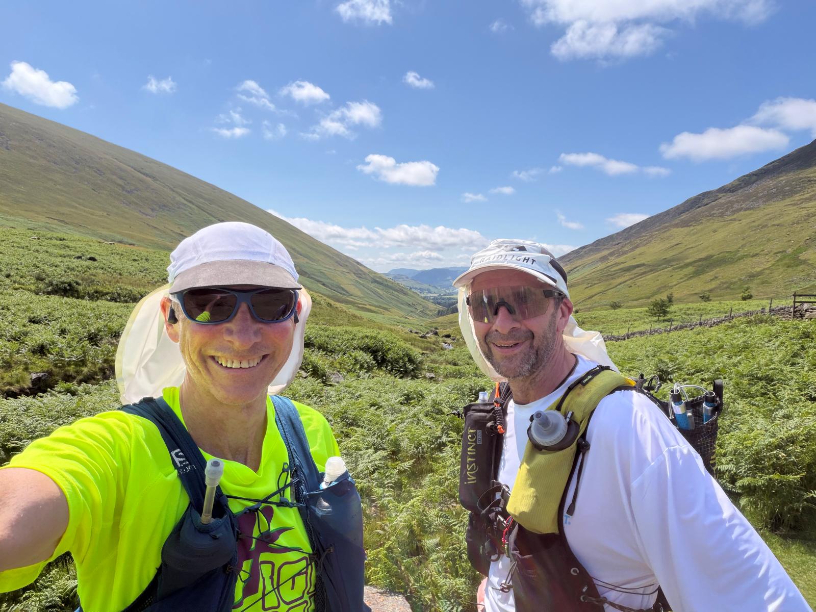 Jim Chris Lakeland Recce jul26 two athletes in the bright sunshine on a Lakeland 100 recce. Wearing peaked hats with sun shades.